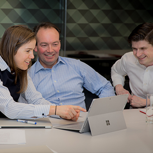 Certa CEO Edward Beckwith and Tax insurance Directors Rachel Hine and Adam Singer are sat, smiling, viewing a tablet together